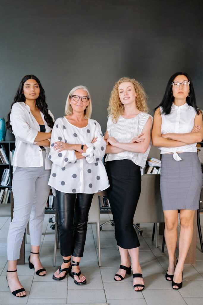 Four diverse businesswomen standing confidently with arms crossed in a modern office setting.